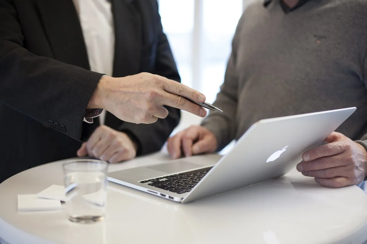 #FotoDescrição: Duas pessoas discutindo algo no laptop durante uma reunião.