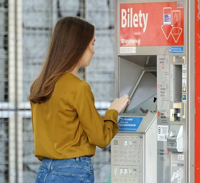 #FotoDescrição: Mulher em frente a uma máquina automática de bilhetes, inserindo dinheiro. Ilustra o conceito de transações e economia com cashback.