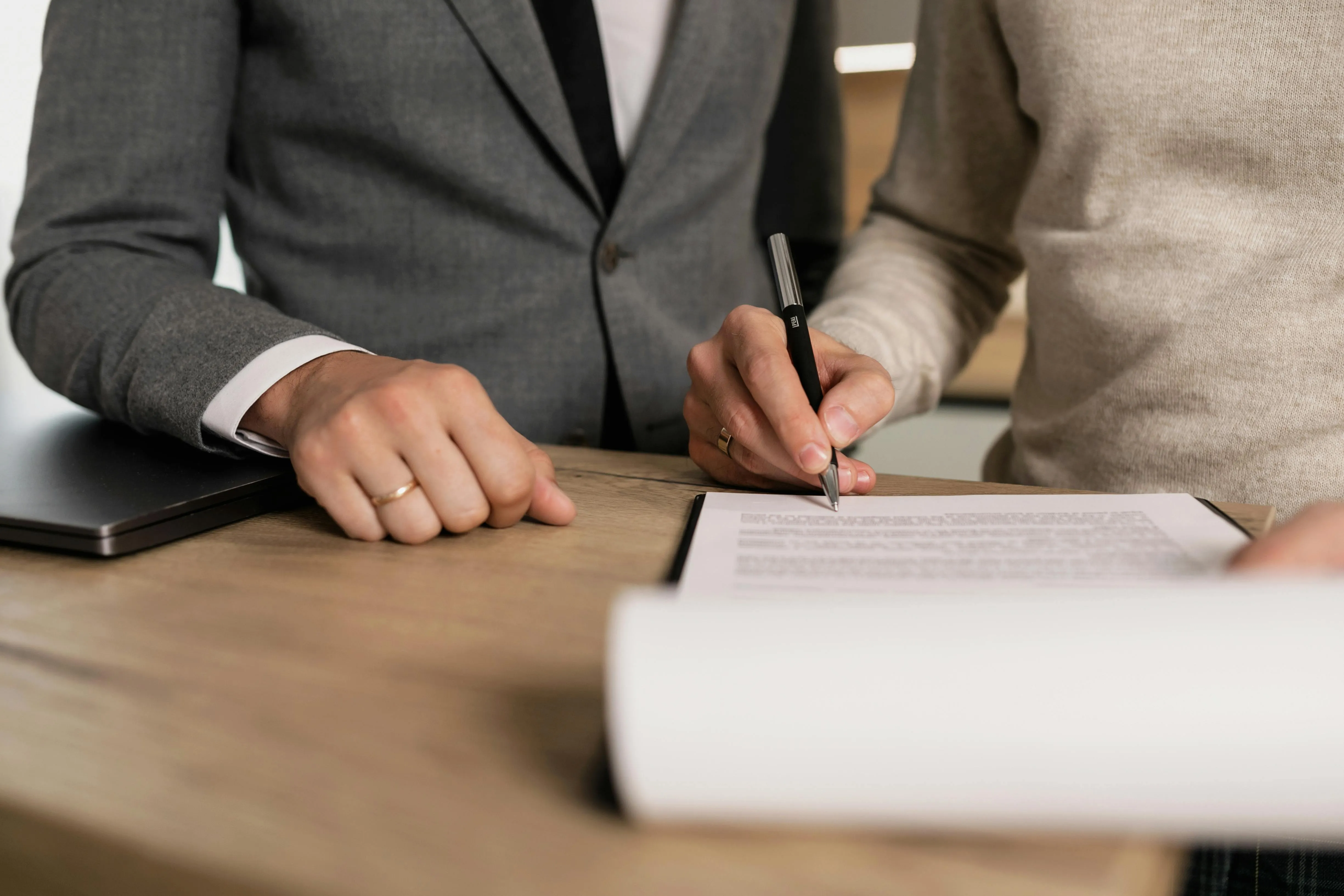 #FotoDescrição: Mãos assinando um contrato em uma mesa de madeira.