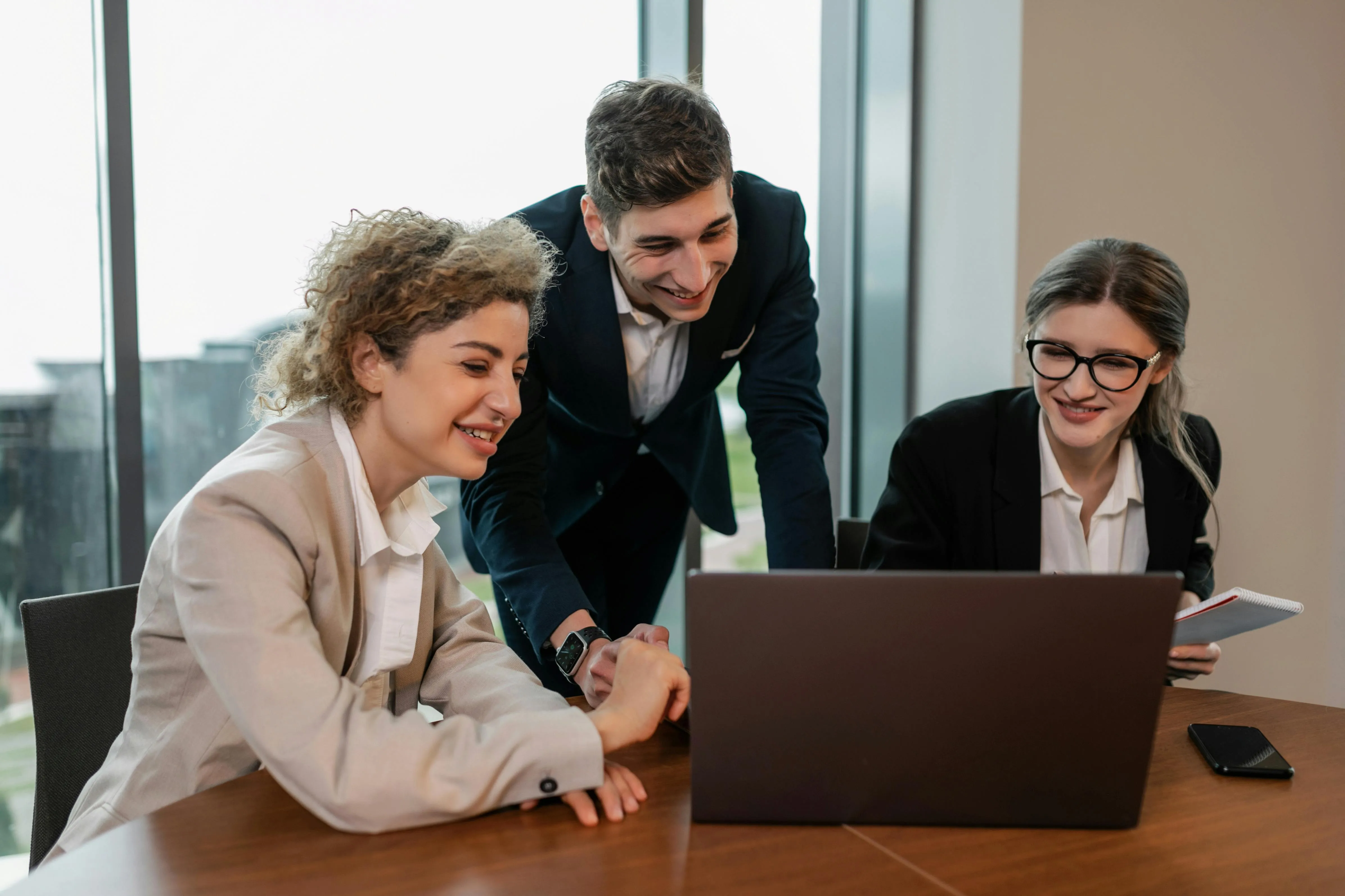 Três pessoas sorrindo colaboram em frente a notebook