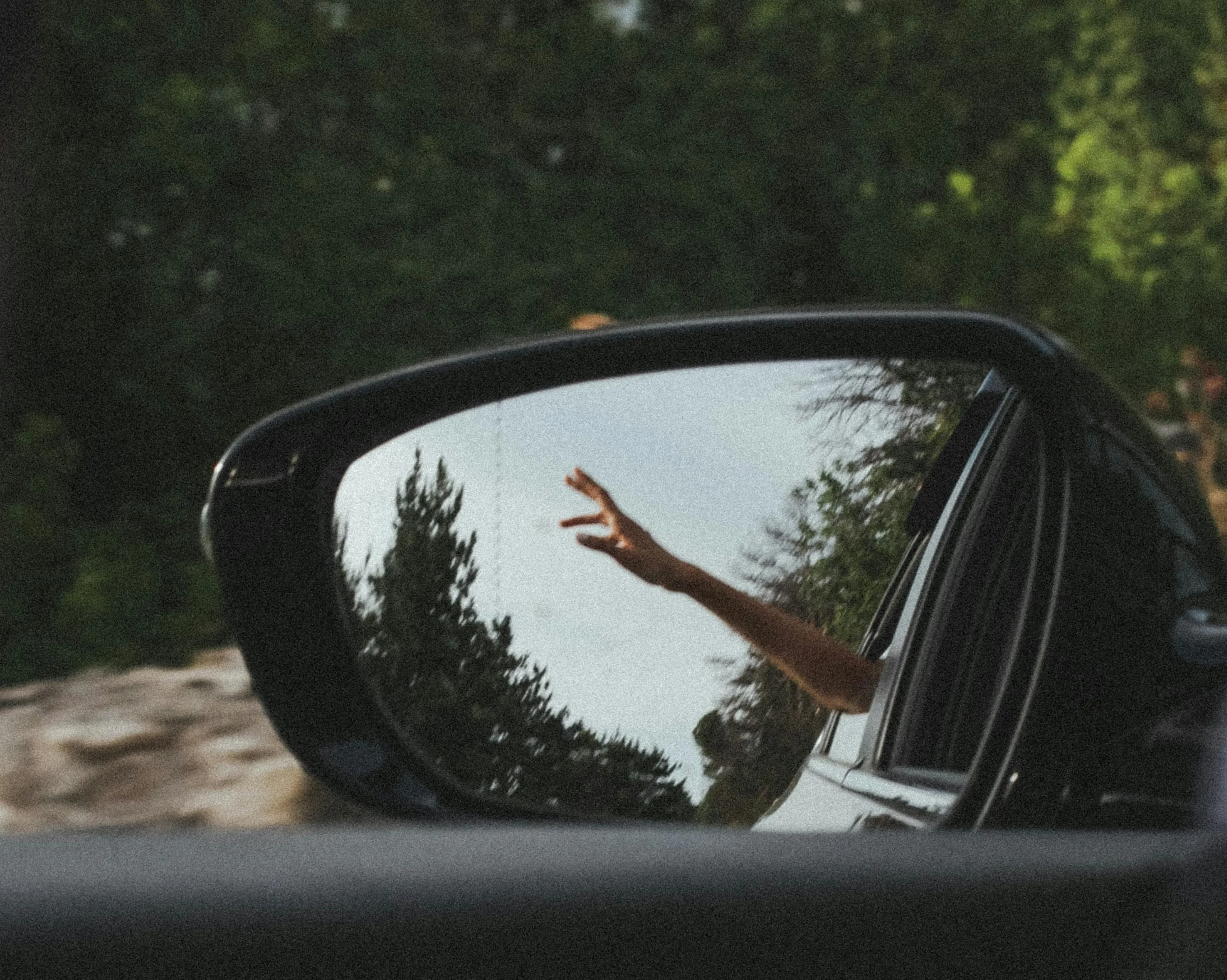 #FotoDescrição Reflexo no espelho retrovisor de um carro com uma mão acenando.