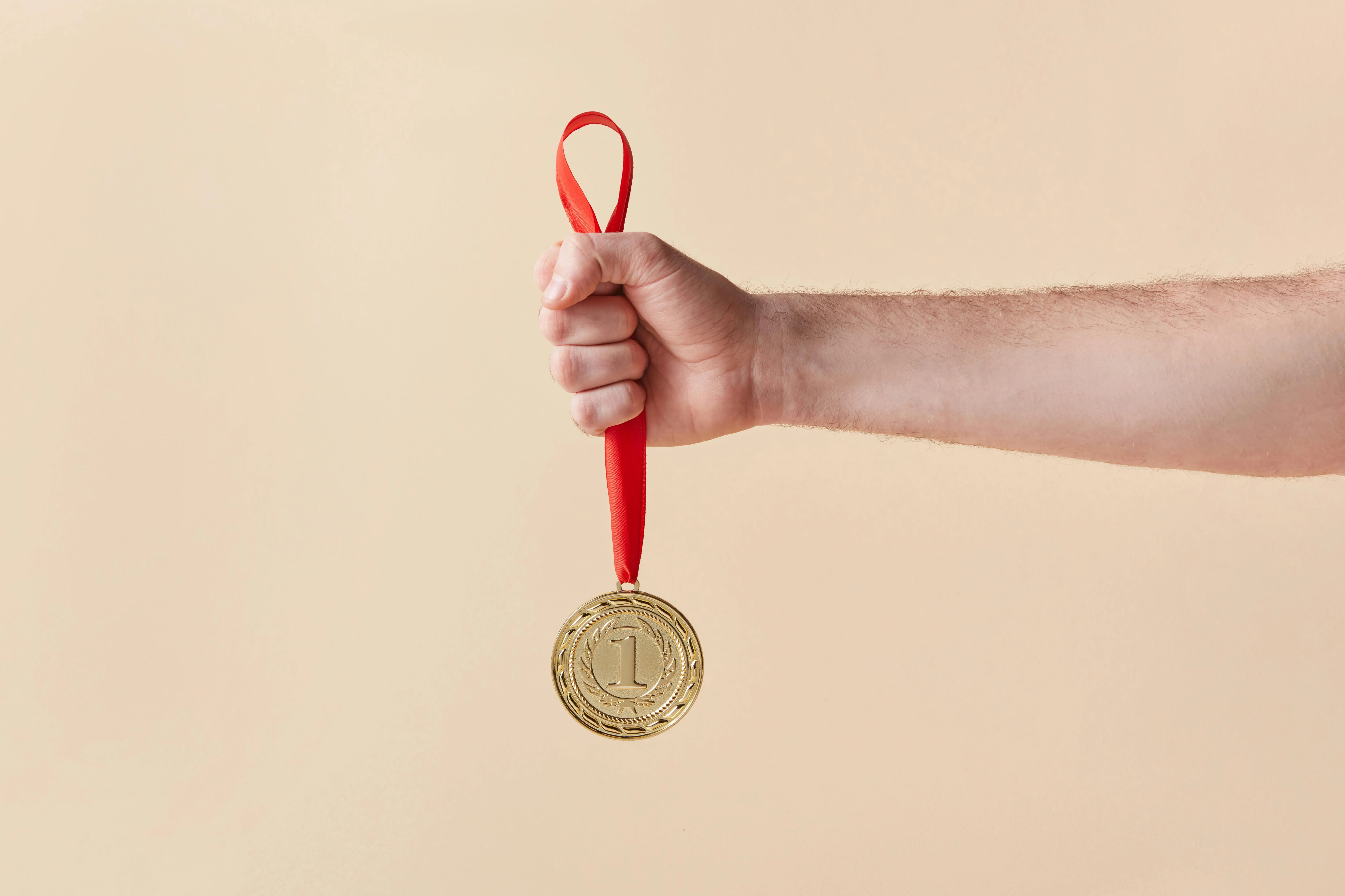 #FotoDescrição: Uma mão segurando uma medalha dourada com fita vermelha, simbolizando vitória e conquistas.