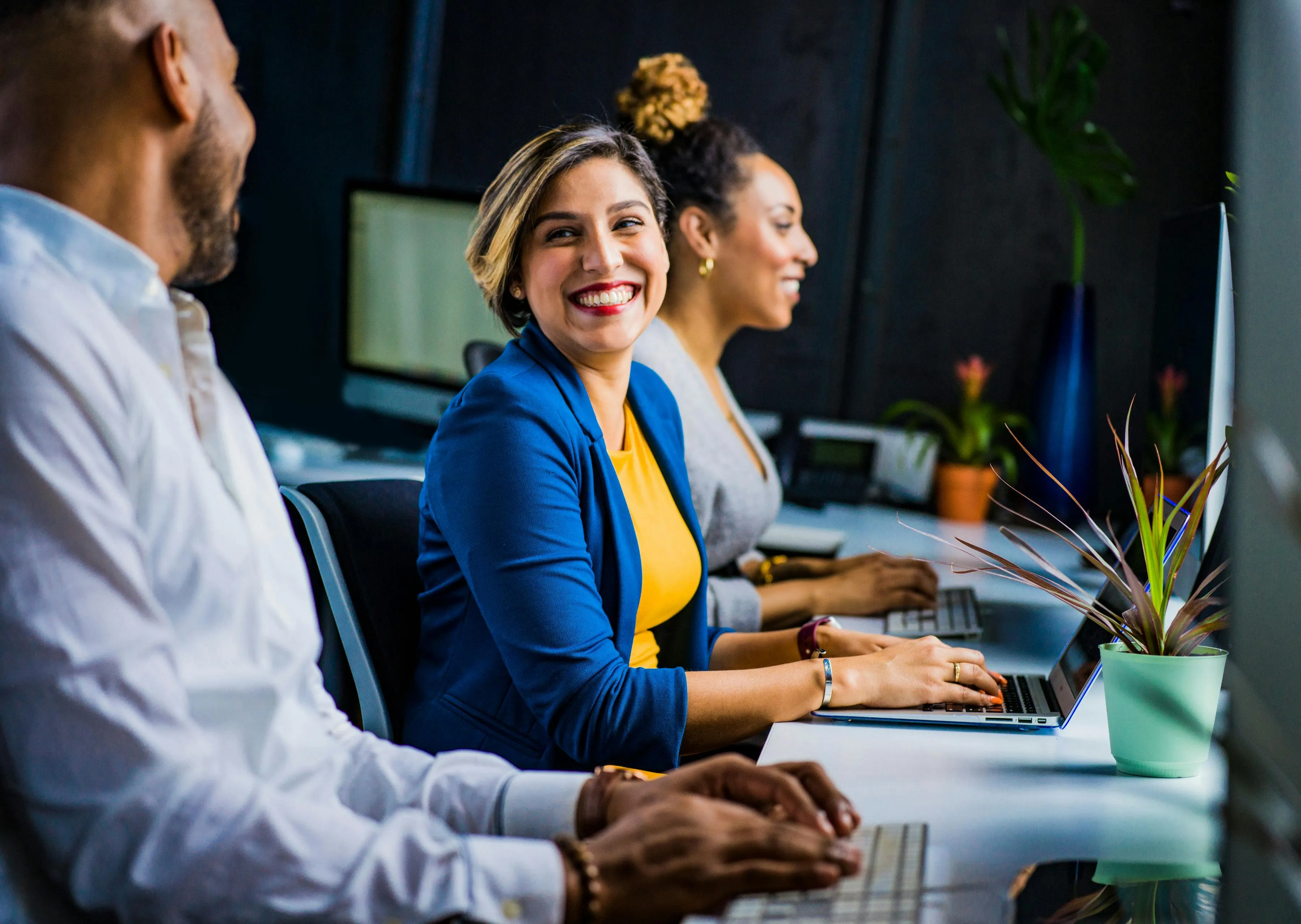 #FotoDescrição: Equipe sorridente trabalhando em computadores em um ambiente moderno.