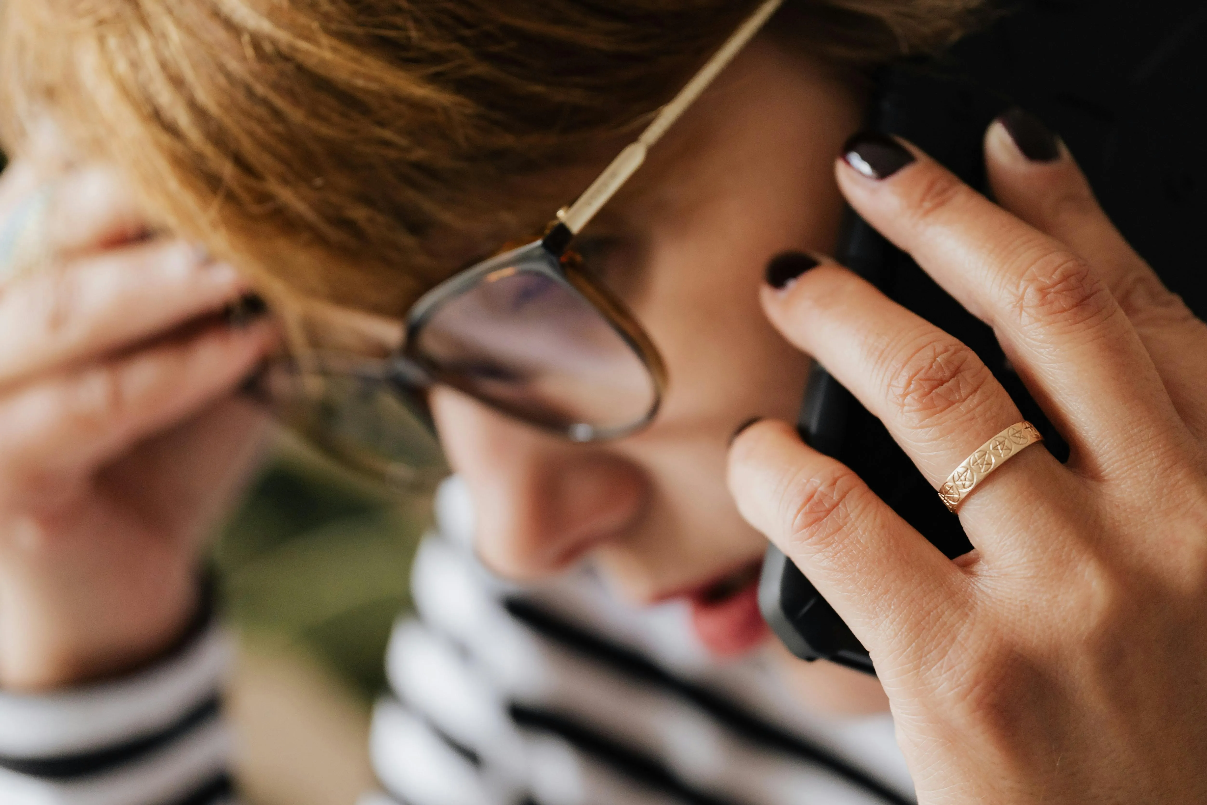 #FotoDescrição Mulher de óculos segurando um telefone próximo ao rosto, com uma expressão preocupada e a mão na testa.