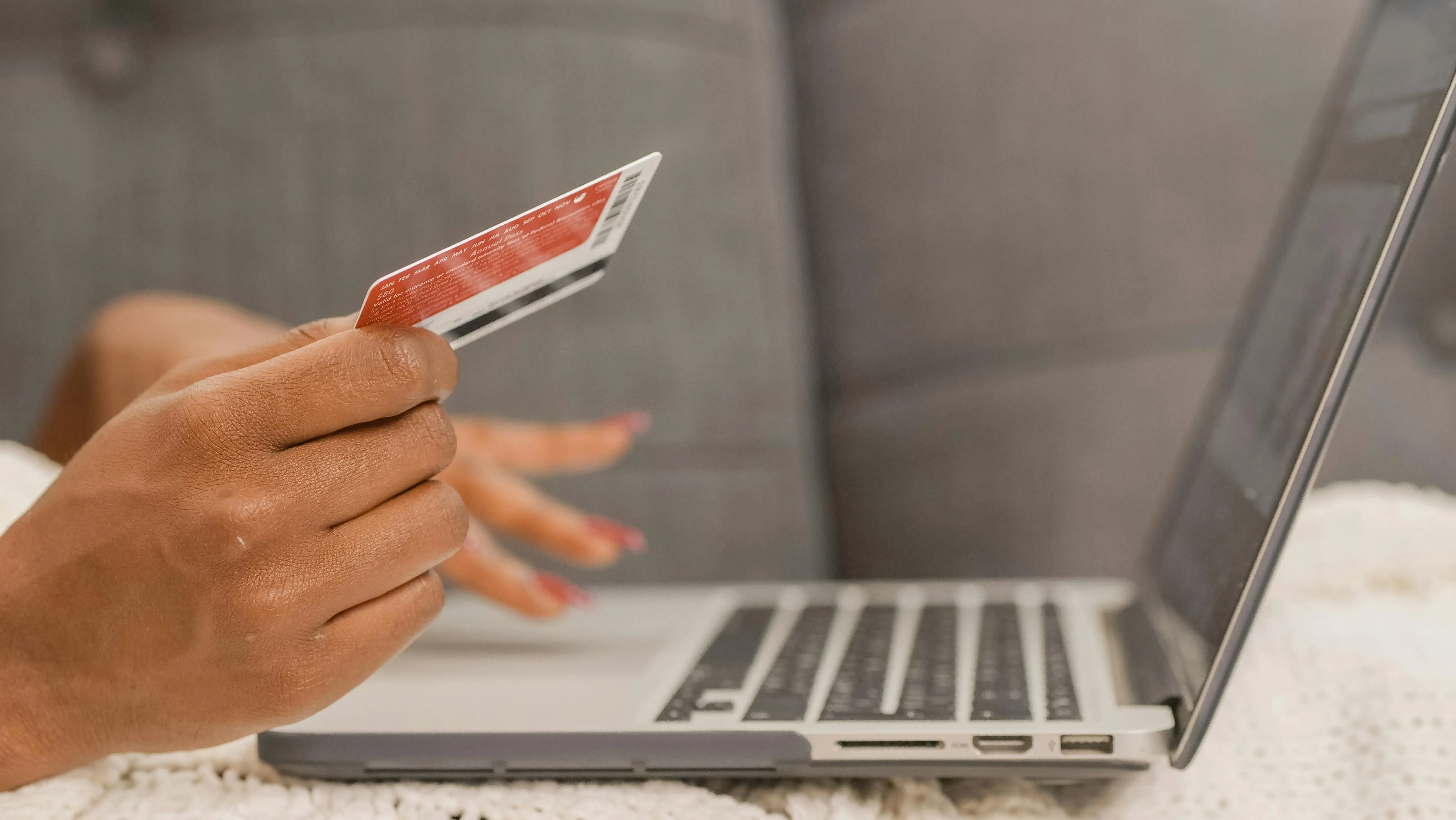 #FotoDescrição: Mão segurando cartão de crédito enquanto faz compras online em um laptop.