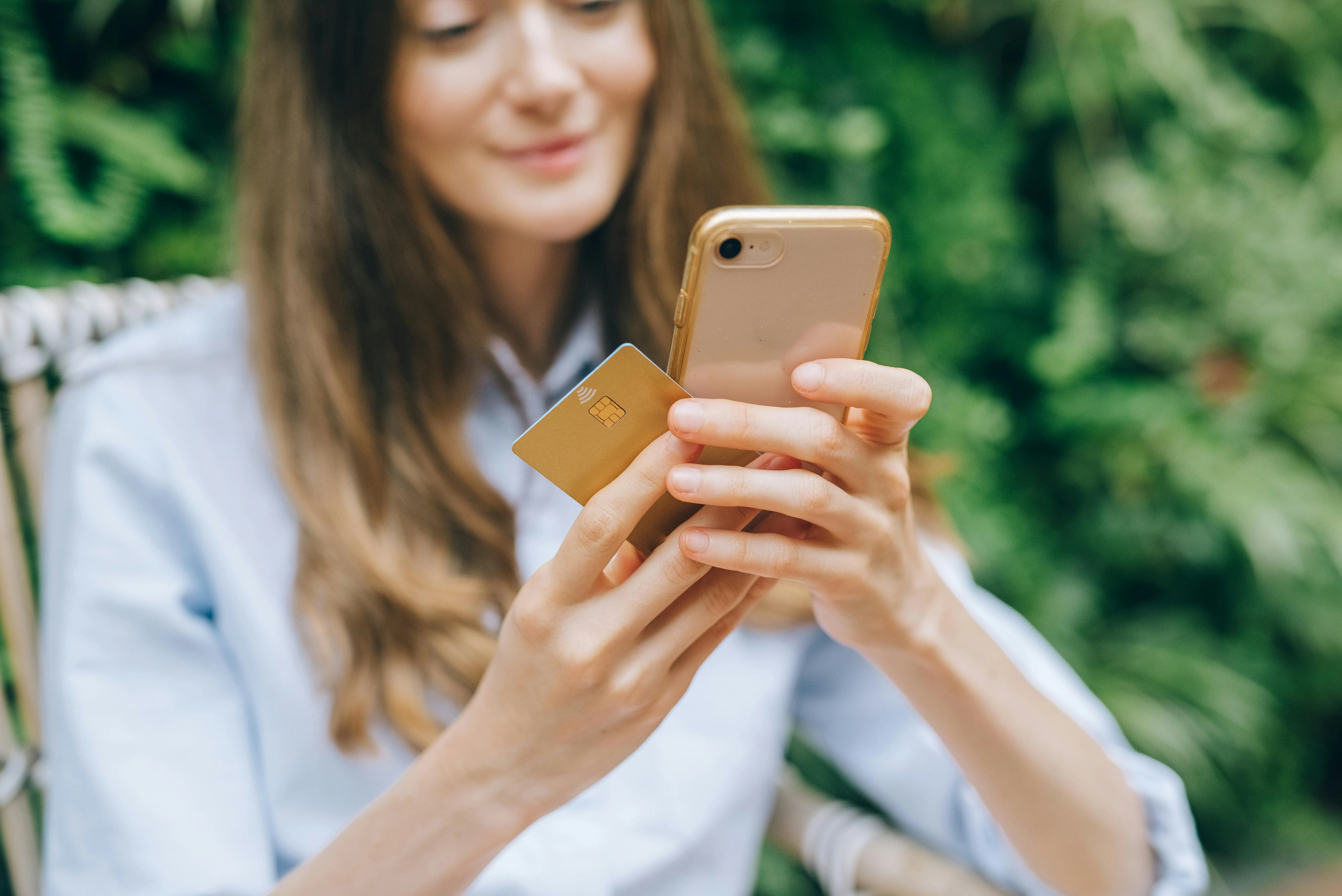 Mulher usando cartão e celular para fazer pagamento online.