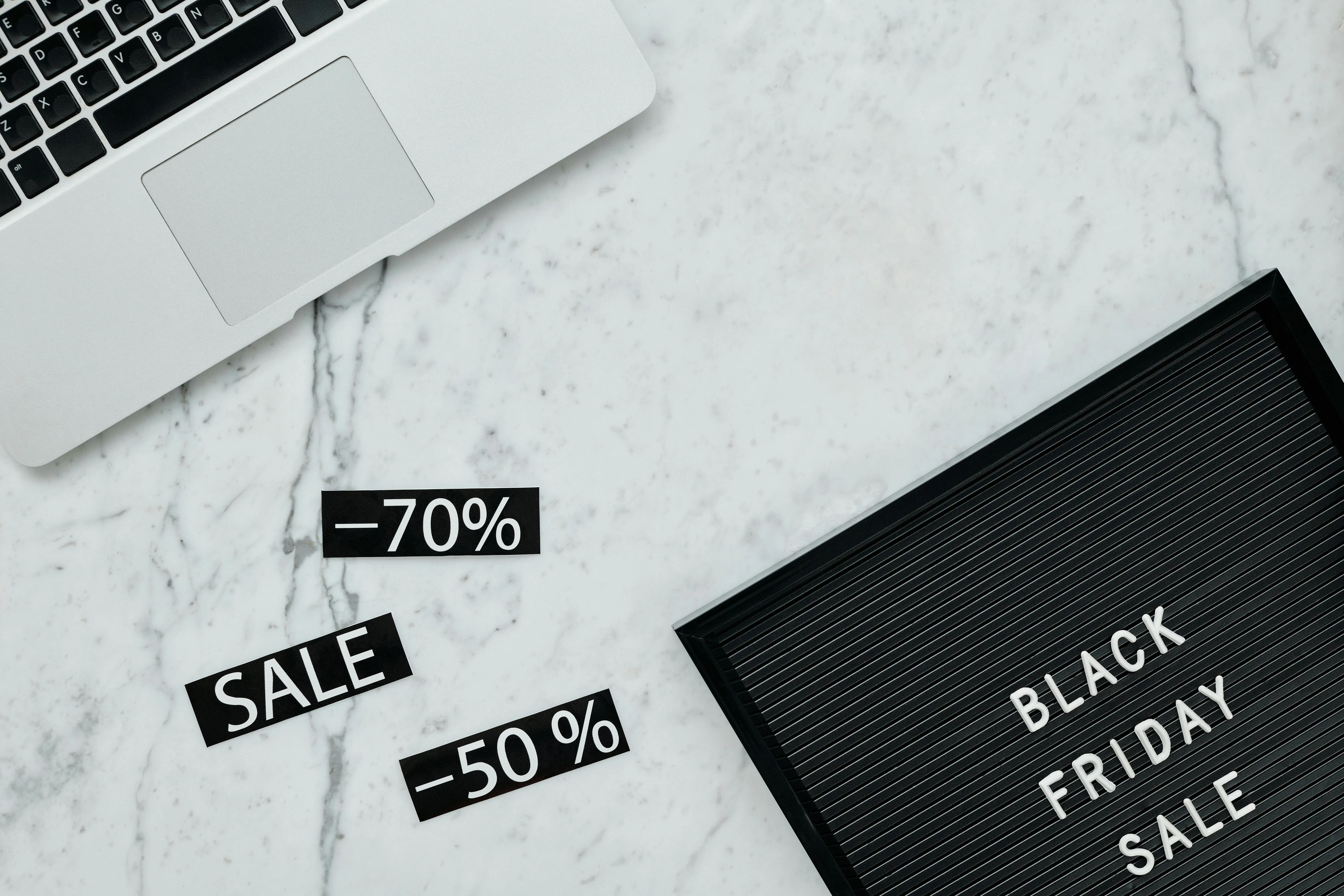 Mesa de mármore com laptop branco, cartaz de descontos e placa 'Black Friday Sale'.