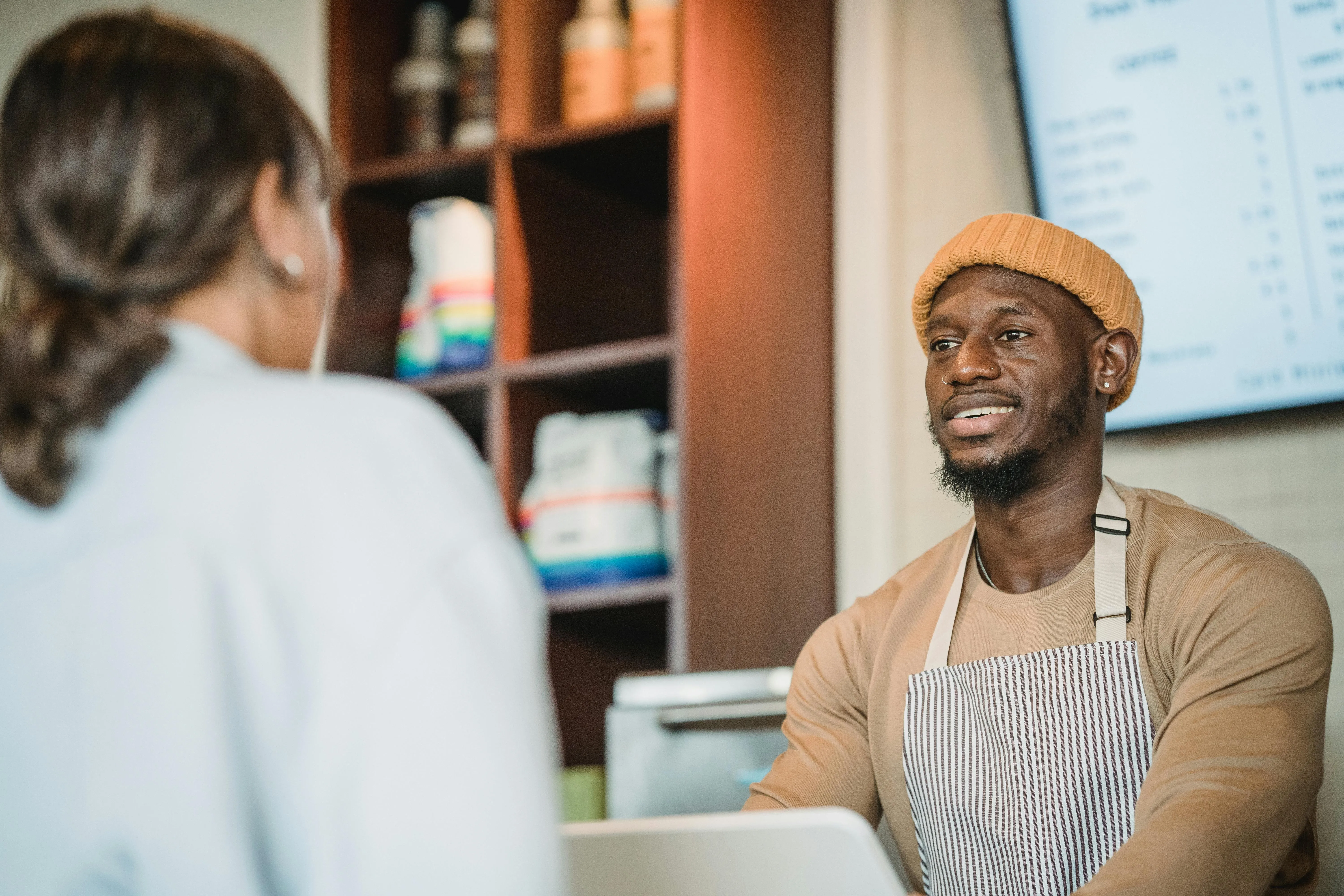 #FotoDescrição: Atendente sorridente conversando com cliente em um balcão de atendimento.