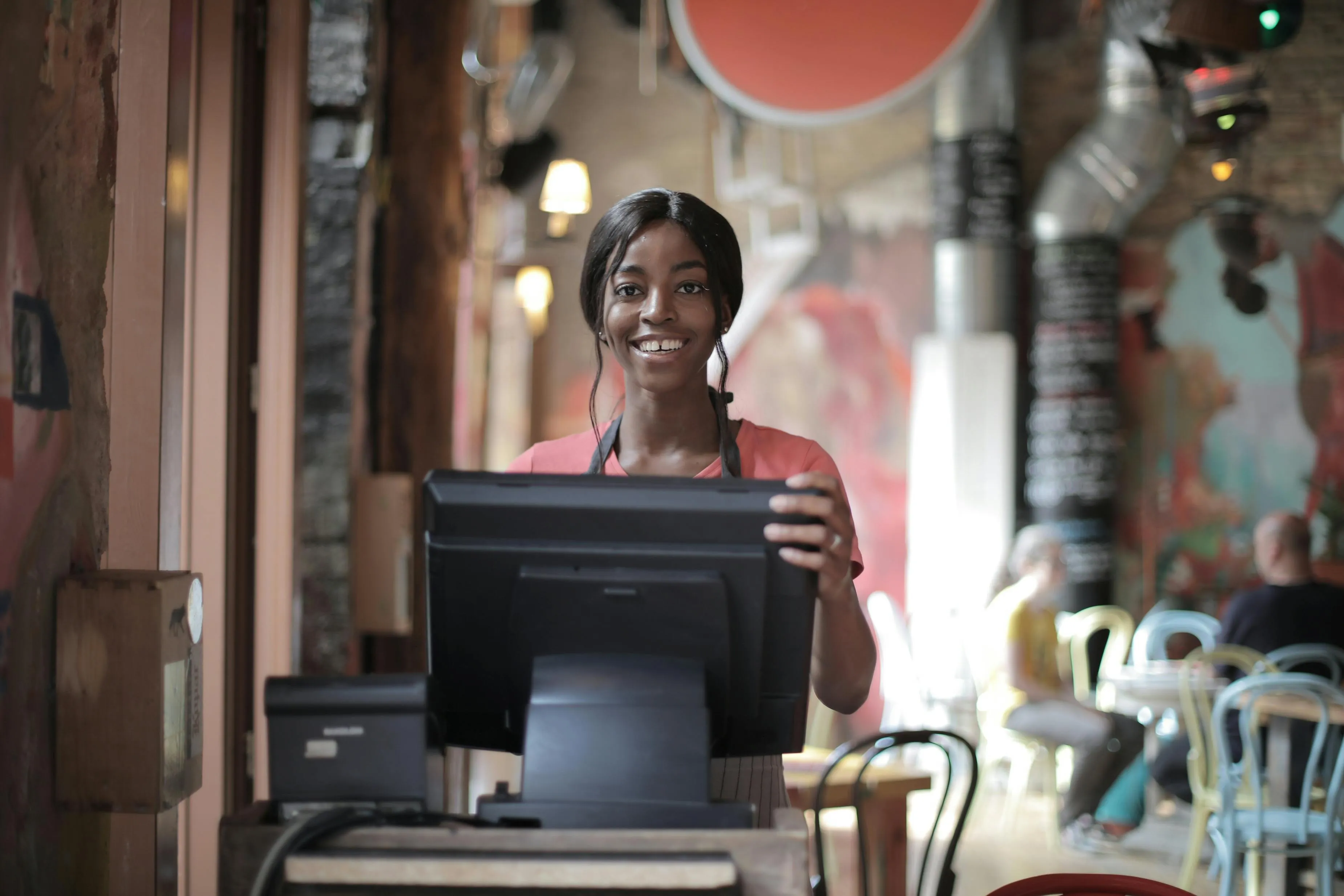 #FotoDescrição: Atendente sorridente no caixa de um restaurante, destacando atendimento ao cliente.