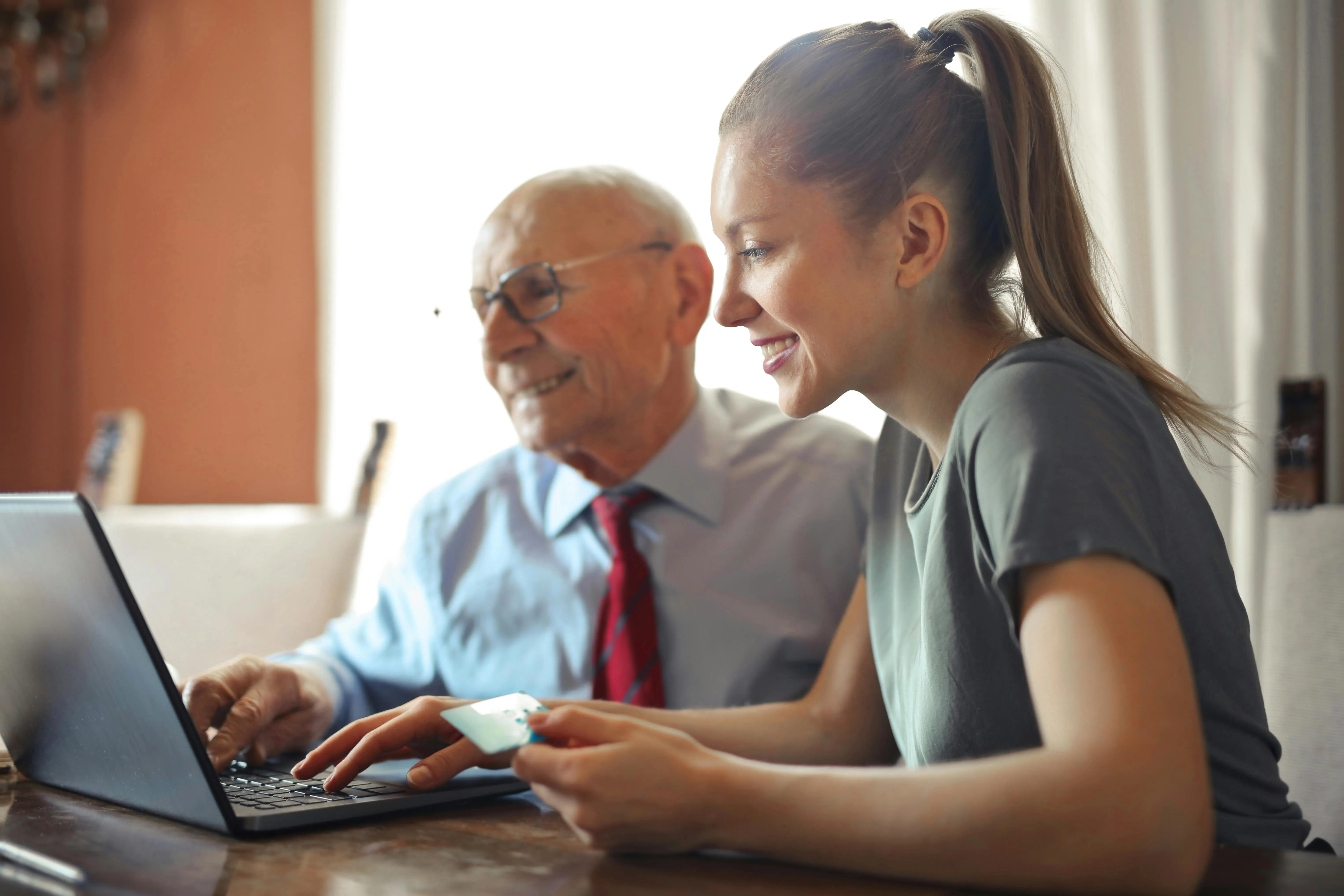 #FotoDescrição: Jovem ajudando um homem mais velho a realizar uma compra online.