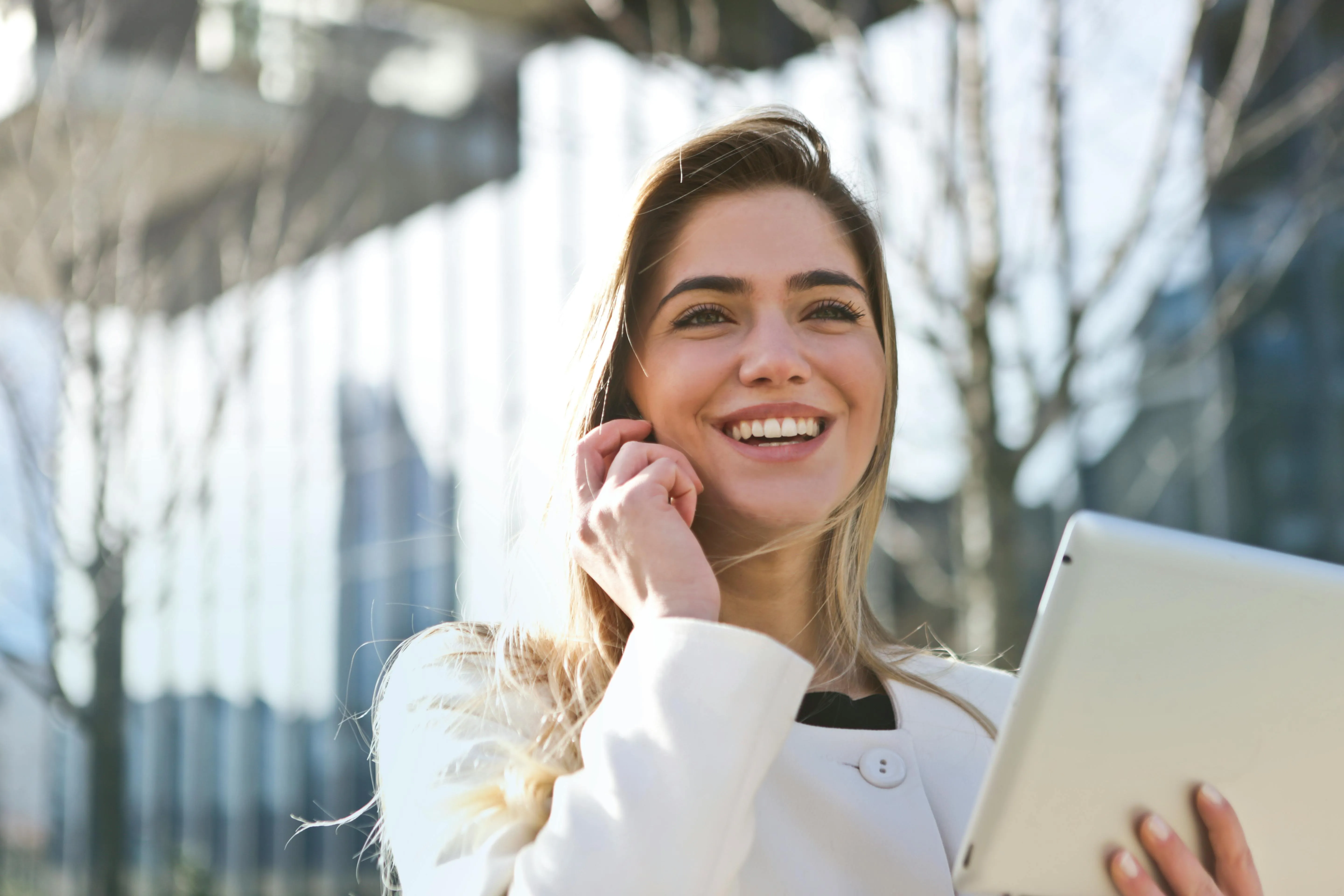 #FotoDescrição Mulher sorrindo ao falar ao telefone enquanto segura um tablet.