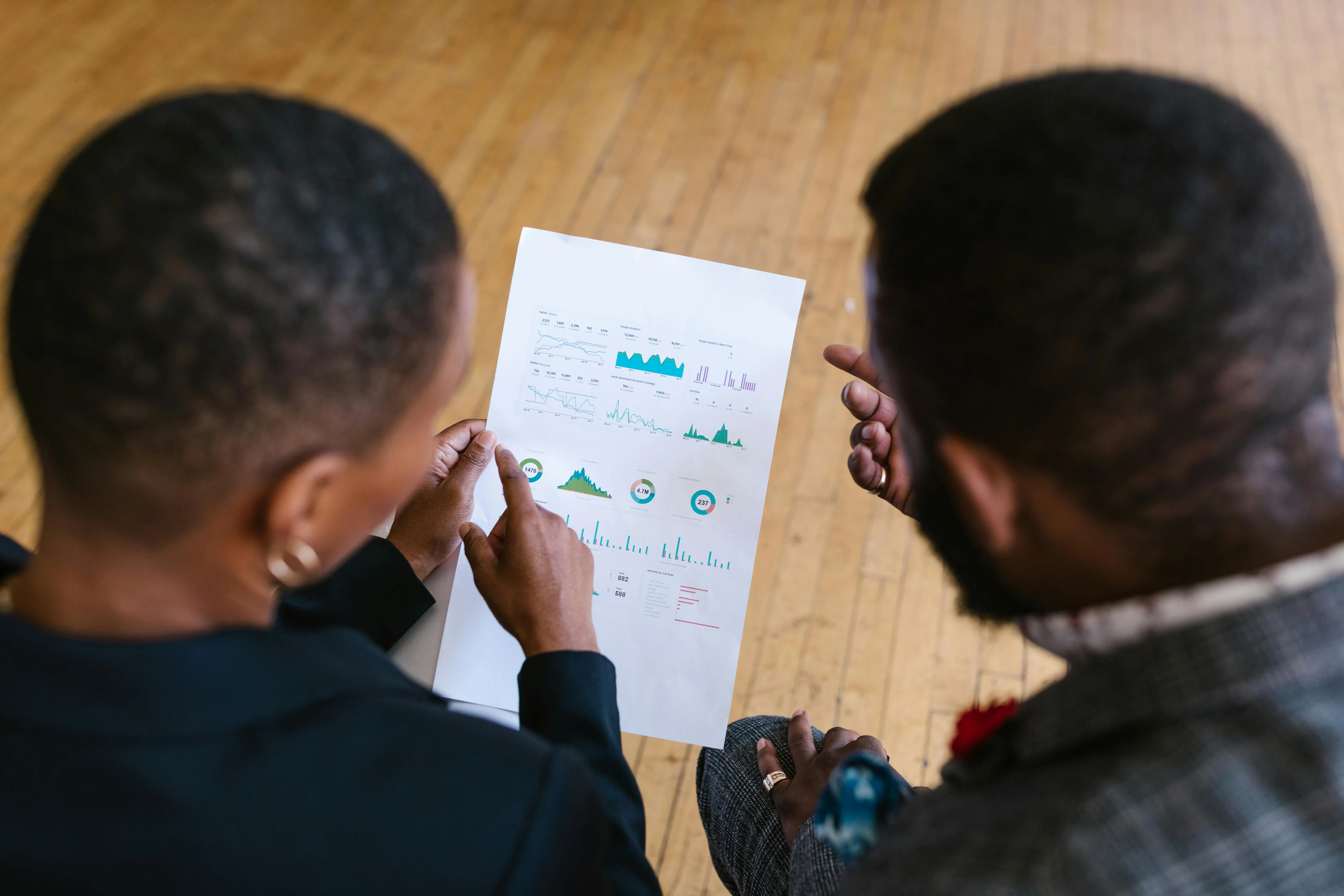 Duas pessoas analisando gráficos e dados em folha impressa.