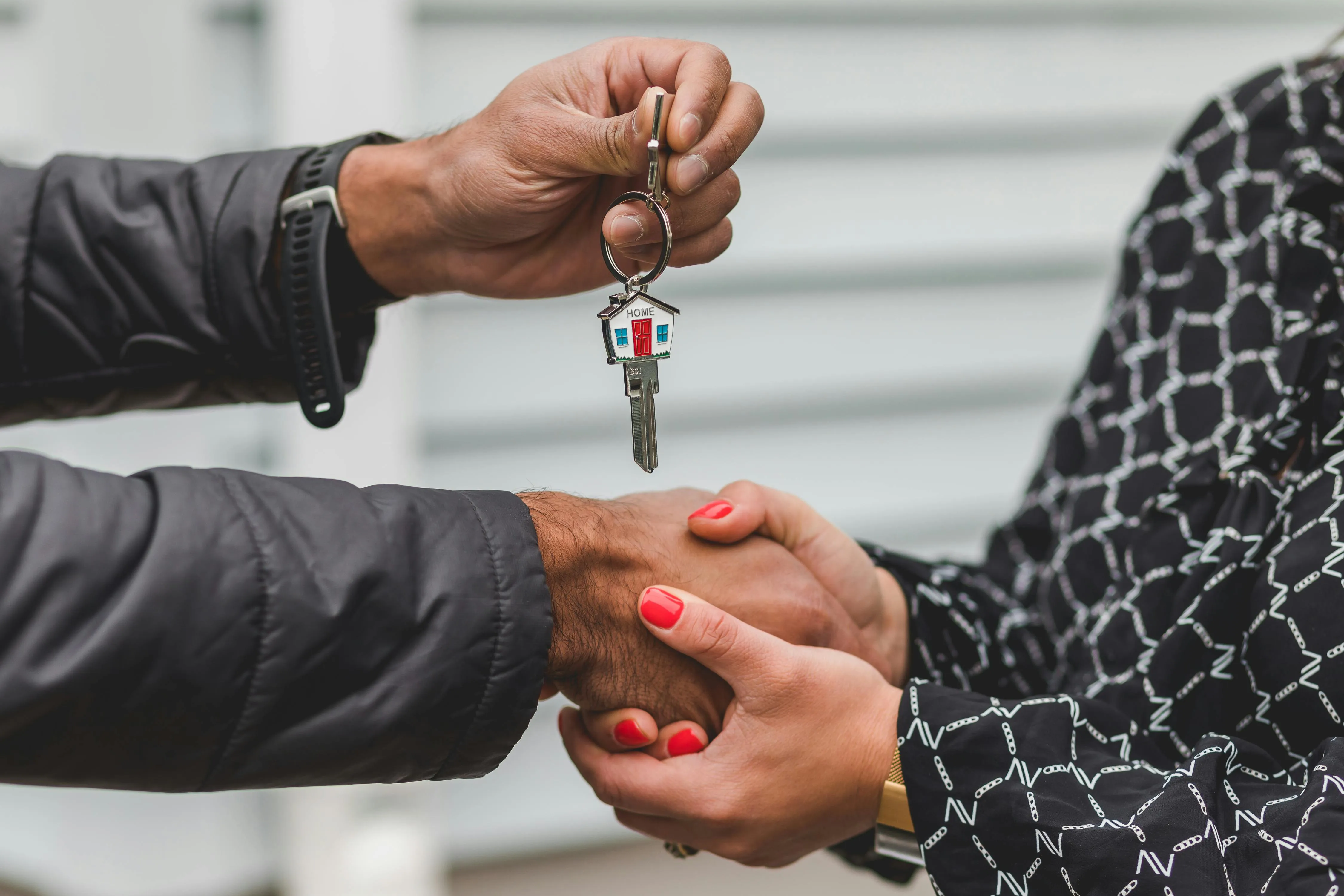 #FotoDescrição: Pessoa entrega a chave de um imóvel com um chaveiro em formato de casa a outra, simbolizando o fechamento de uma venda ou locação residencial.