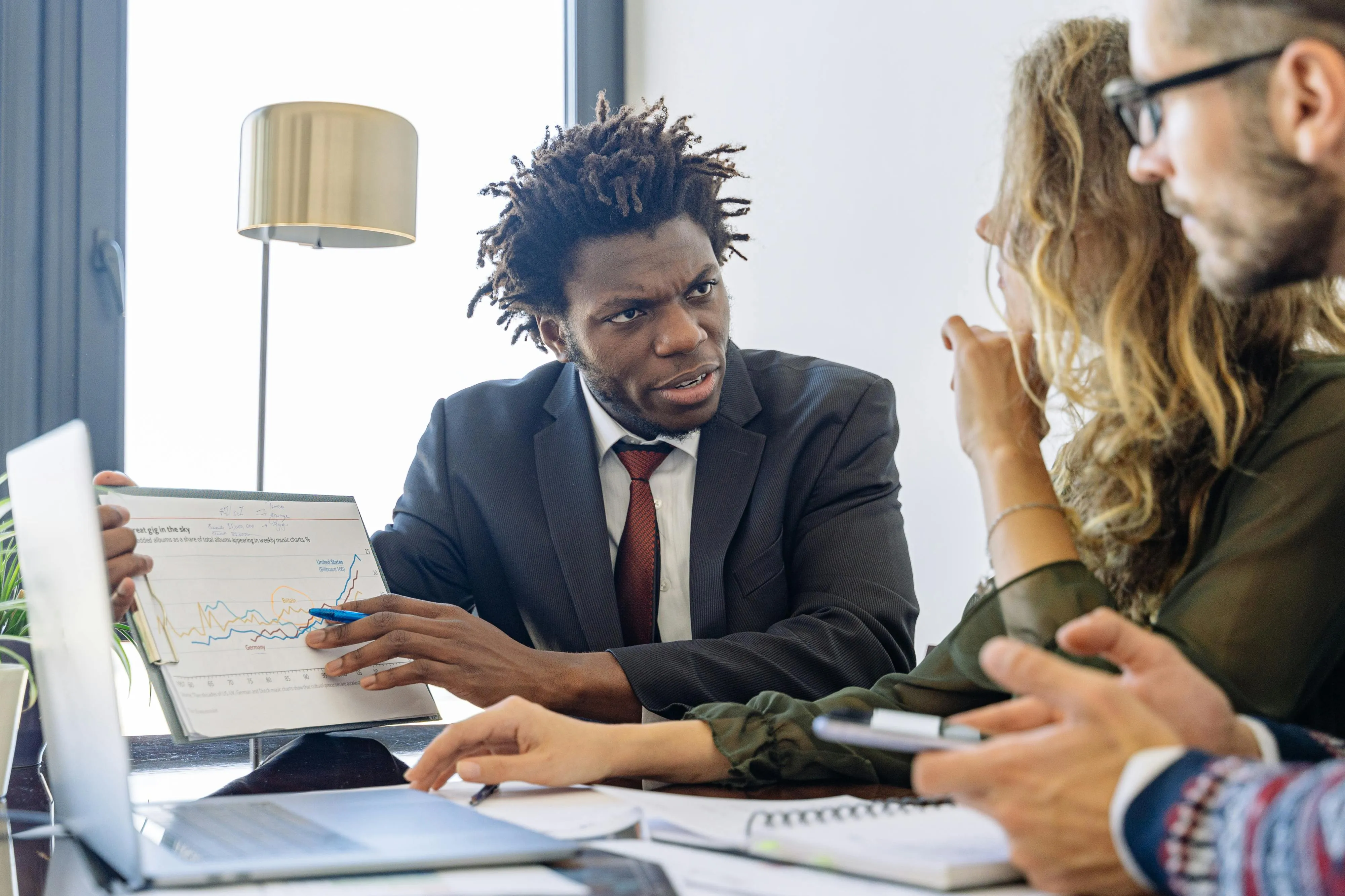 Três profissionais em reunião de negócios, discutindo estratégias e dados em escritório moderno.