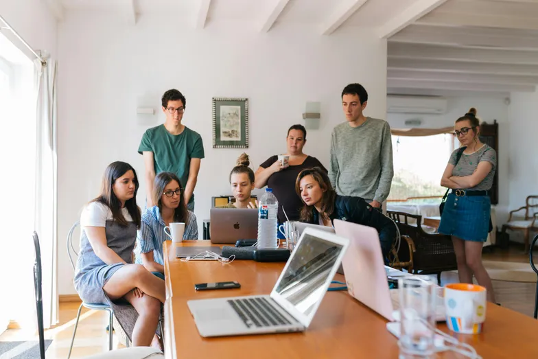 Grupo de pessoas reunido em volta de mesa olhando para um notebook.