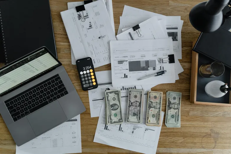 #FotoDescrição: Uma mesa com papéis organizados, um notebook, notas de dinheiro e uma calculadora. Representa planejamento financeiro e gestão.