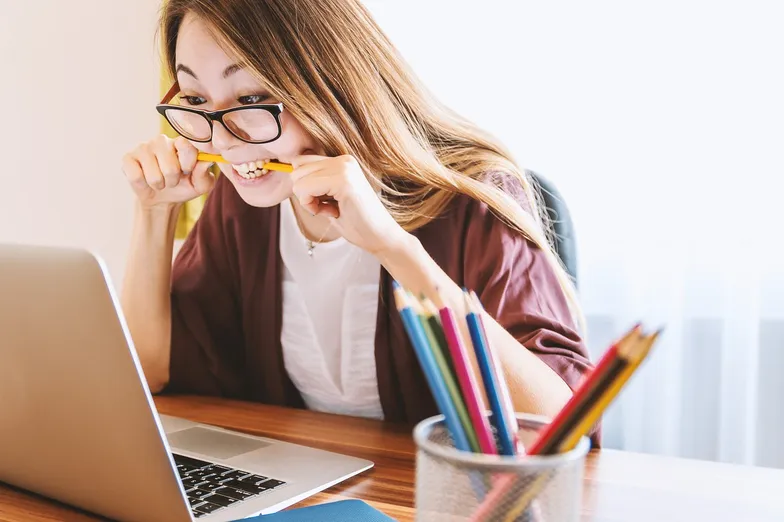 #FotoDescrição: Mulher estressada mordendo um lápis enquanto olha para a tela do laptop