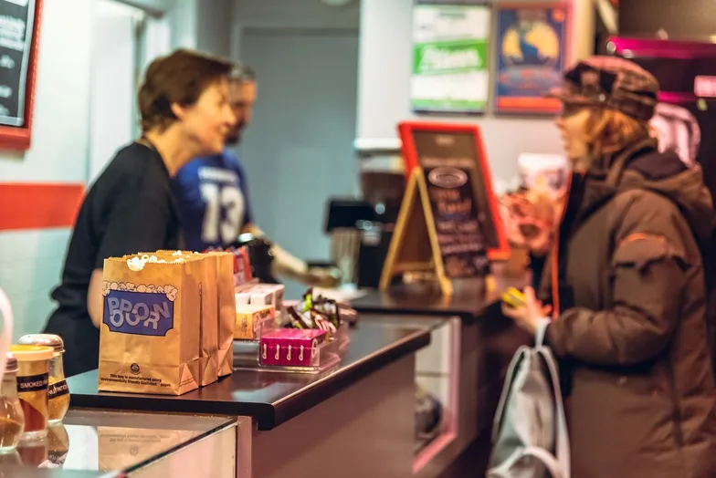 #FotoDescrição: Cliente sendo atendida em balcão de loja, com sacola de compras em destaque.