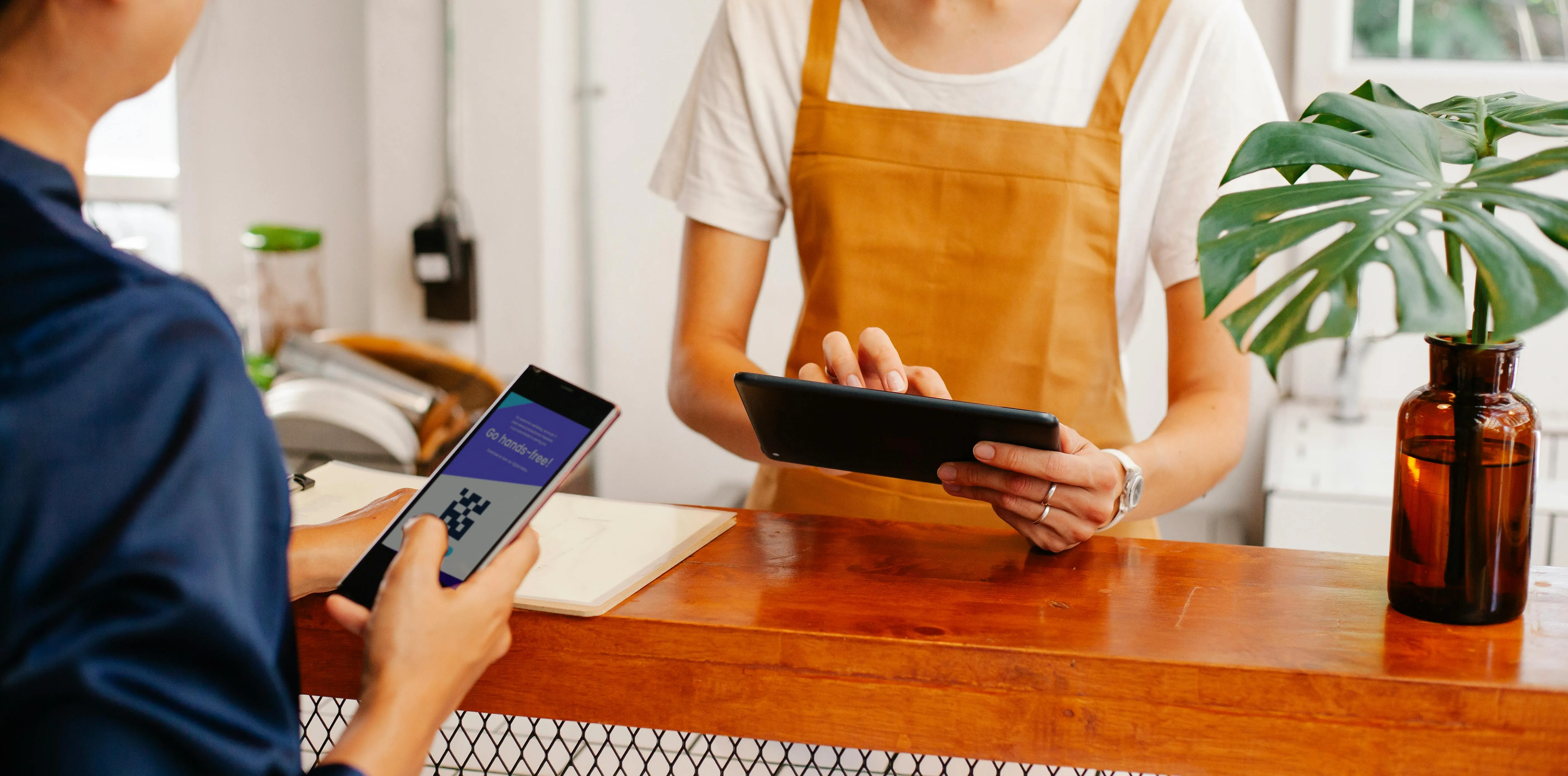 Pagamento por celular em restaurante aconchegante, atendente usa tablet no balcão.