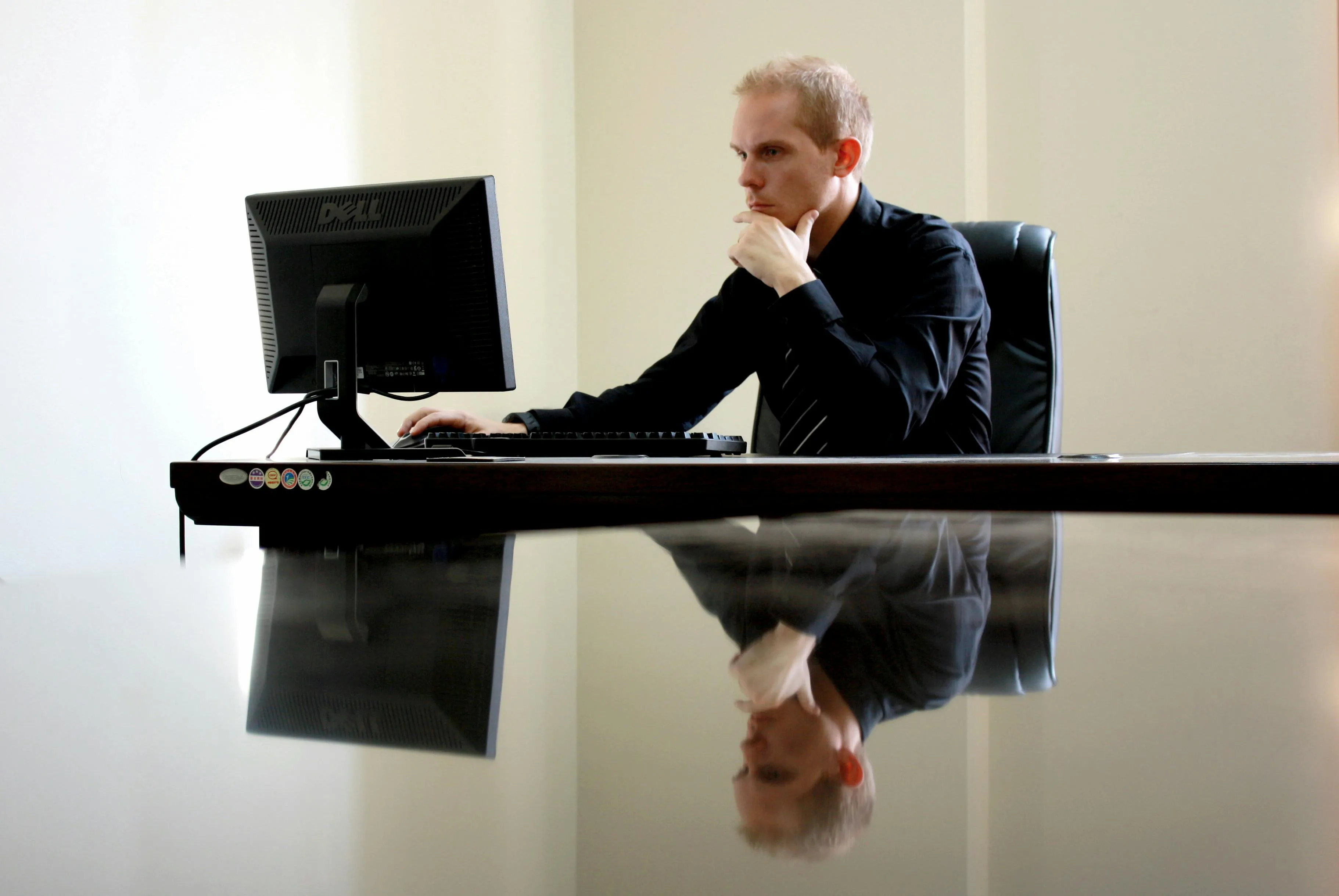 Profissional focado no computador em escritório moderno, refletido na mesa brilhante.