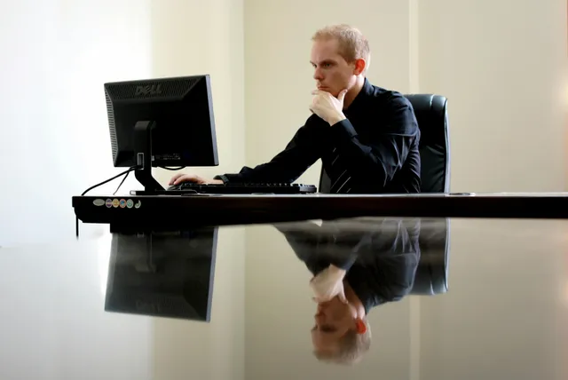 Profissional focado no computador em escritório moderno, refletido na mesa brilhante.