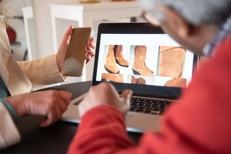 Clientes analisam botas em notebook e celular durante compra online
