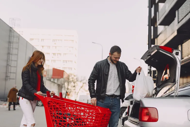 Casal carrega compras do supermercado para o porta-malas do carro.