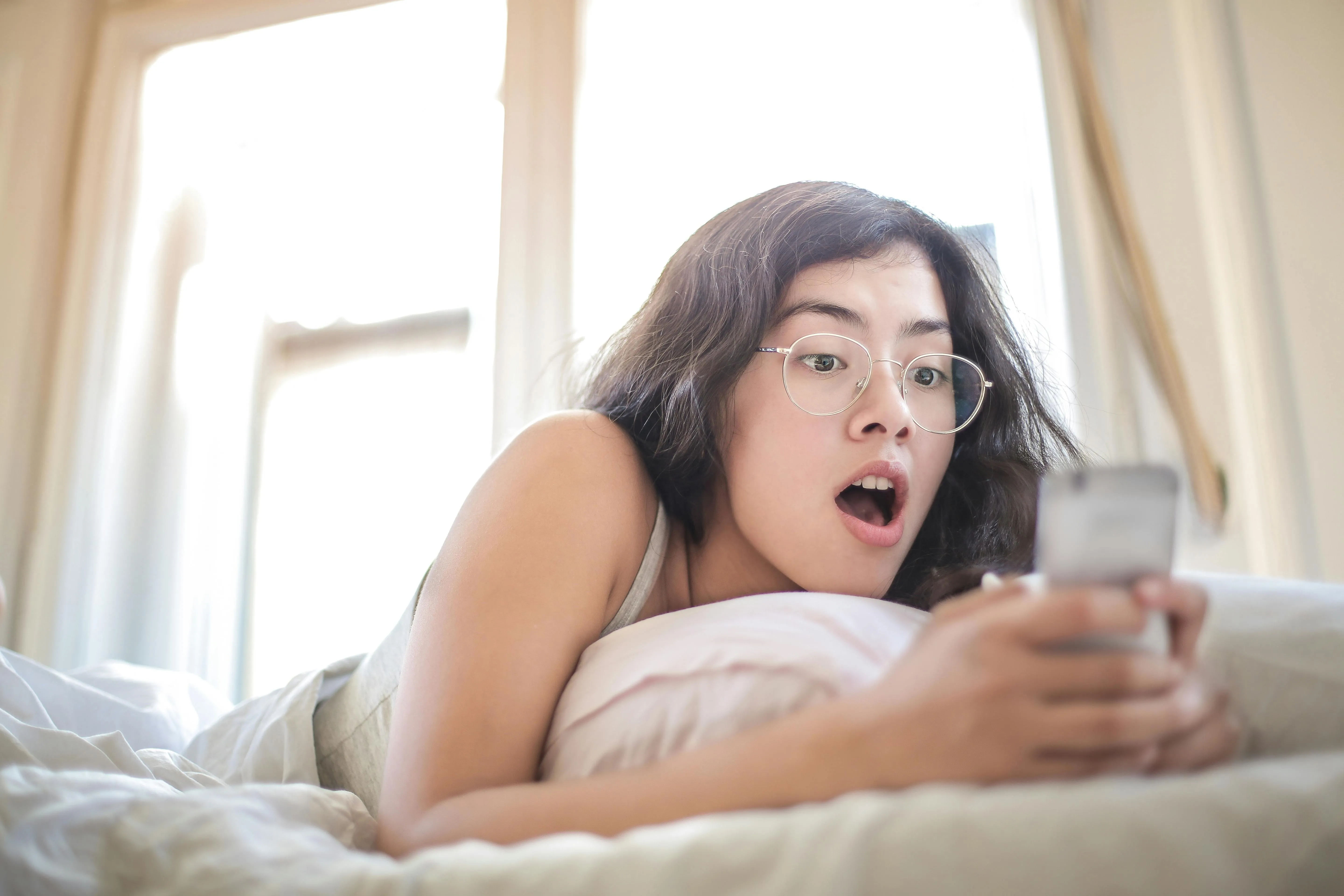 Mulher surpresa olhando para o celular enquanto está deitada.