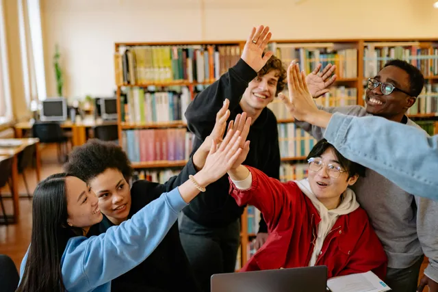 Grupo diverso de estudantes comemora com um high five na biblioteca.