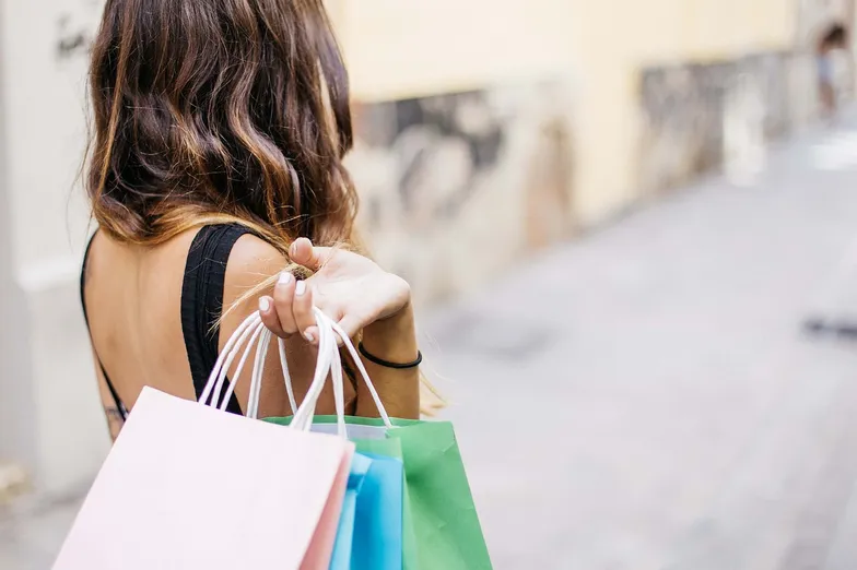 #FotoDescrição: Mulher com sacolas de compras coloridas caminhando em uma rua.