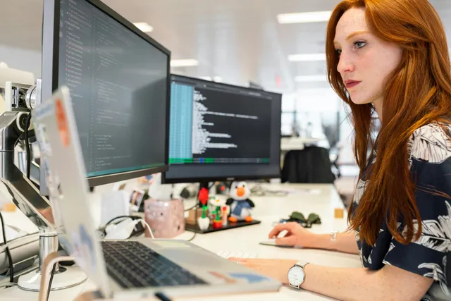 Mulher programando em computador com dois monitores no escritório.