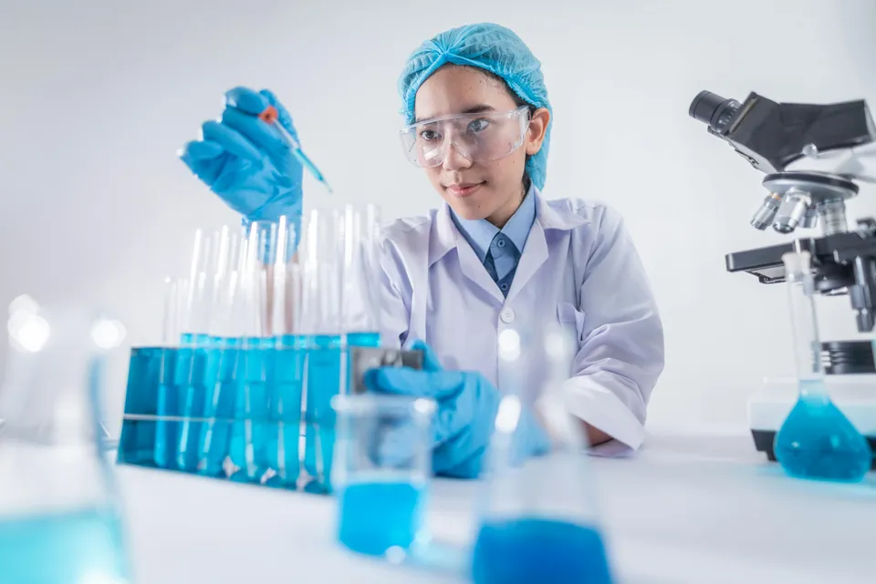 Cientista manuseia tubos de ensaio com líquido azul em laboratório.
