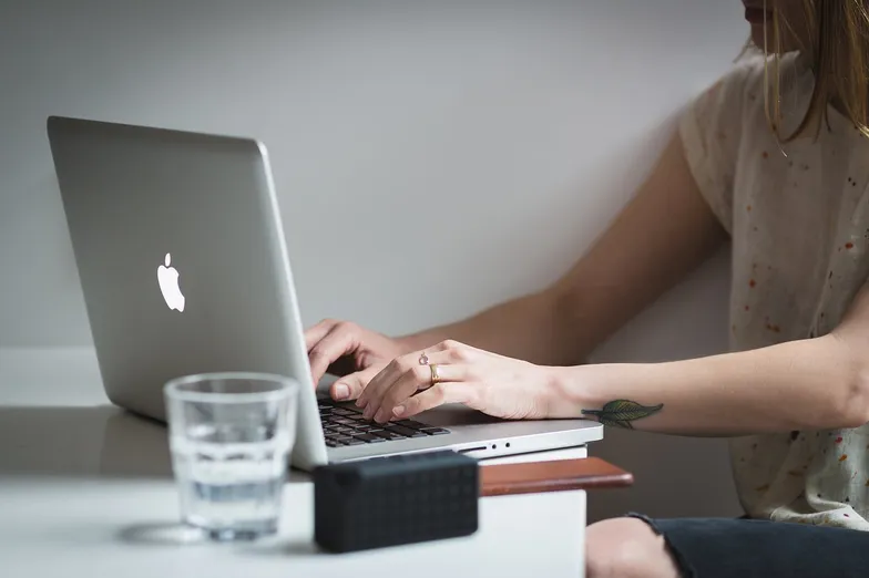 #FotoDescrição: Pessoa digitando em um notebook ao lado de um copo d'água.