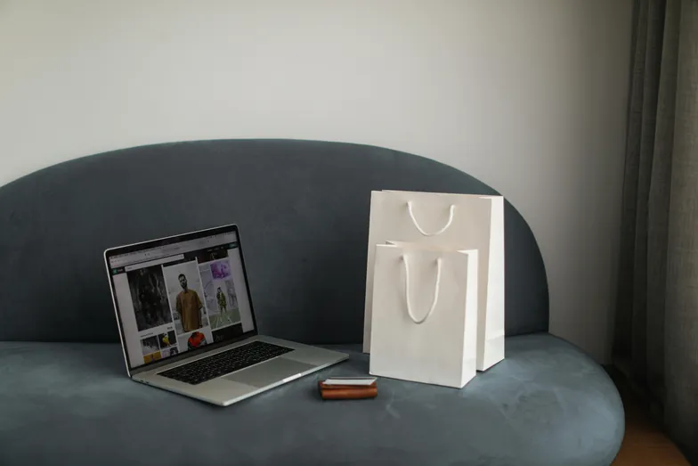 Notebook com compras online e sacolas sobre sofá