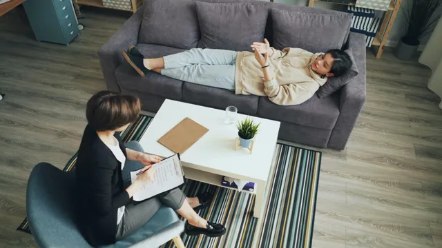 #FotoDescrição: Pessoa deitada em um sofá conversando com uma terapeuta que faz anotações em um caderno durante uma sessão de atendimento em consultório.