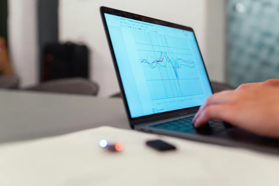 Pessoa analisa gráficos financeiros em notebook sobre uma mesa.