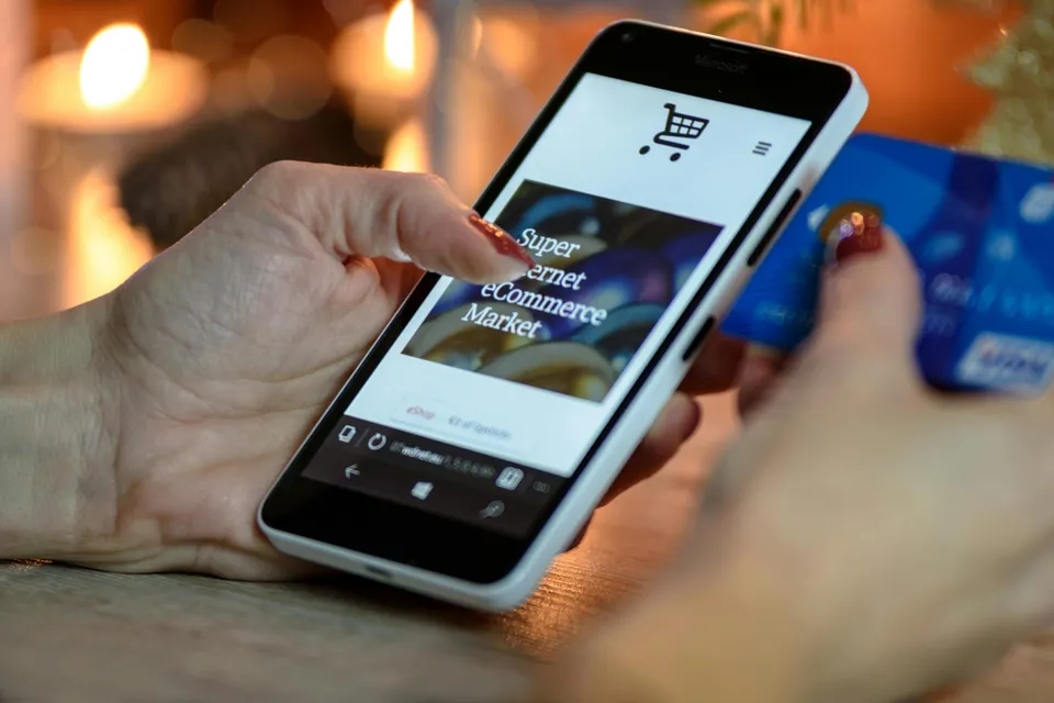 Pessoa compra online pelo celular segurando cartão de crédito.