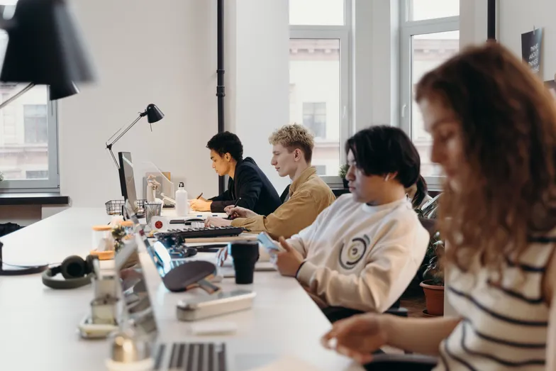 Equipe trabalhando em escritório compartilhado com computadores e celulares.