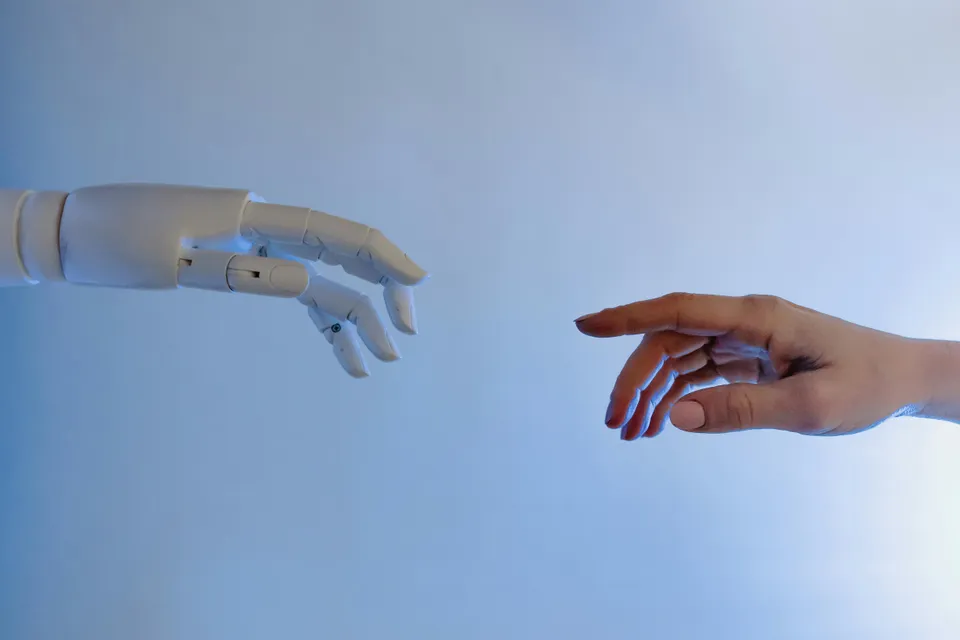 Mão robótica e mão humana quase se tocando, simbolizando conexão humano-IA