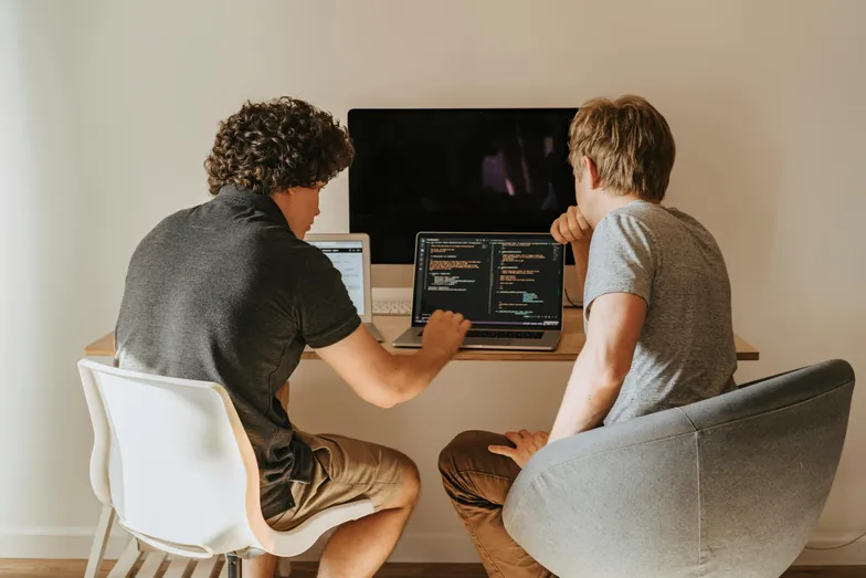 Duas pessoas programando juntas em laptops em ambiente de trabalho