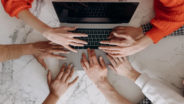 Mãos de várias pessoas usando um notebook sobre mesa de mármore.