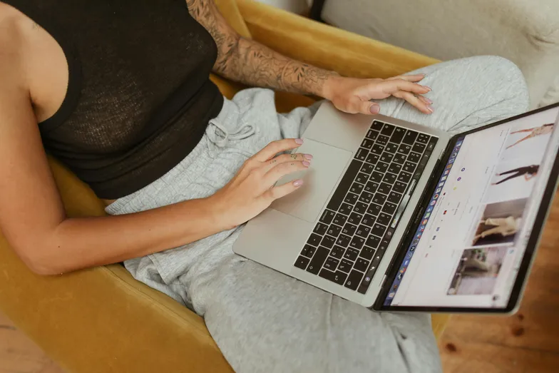 Pessoa sentada em poltrona navegando em site de roupas pelo notebook.