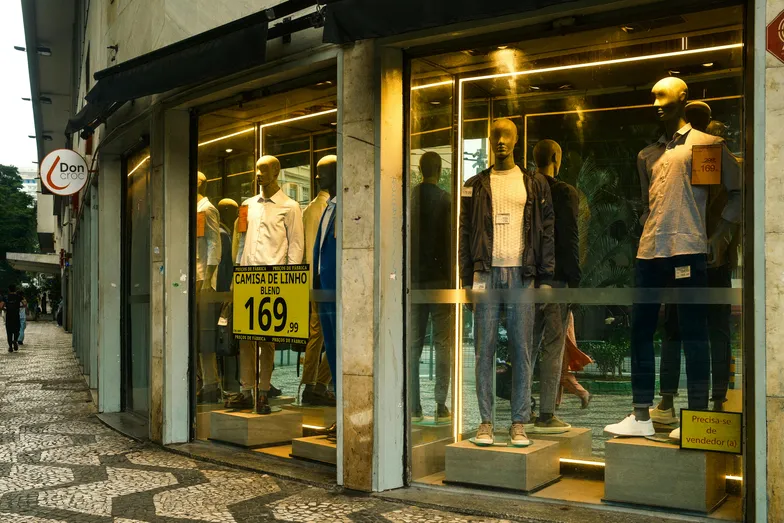 Vitrine de loja com manequins e placas de preço na calçada
