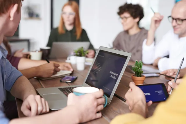 Grupo em reunião com laptops e tablets mostrando gráficos e anotações.