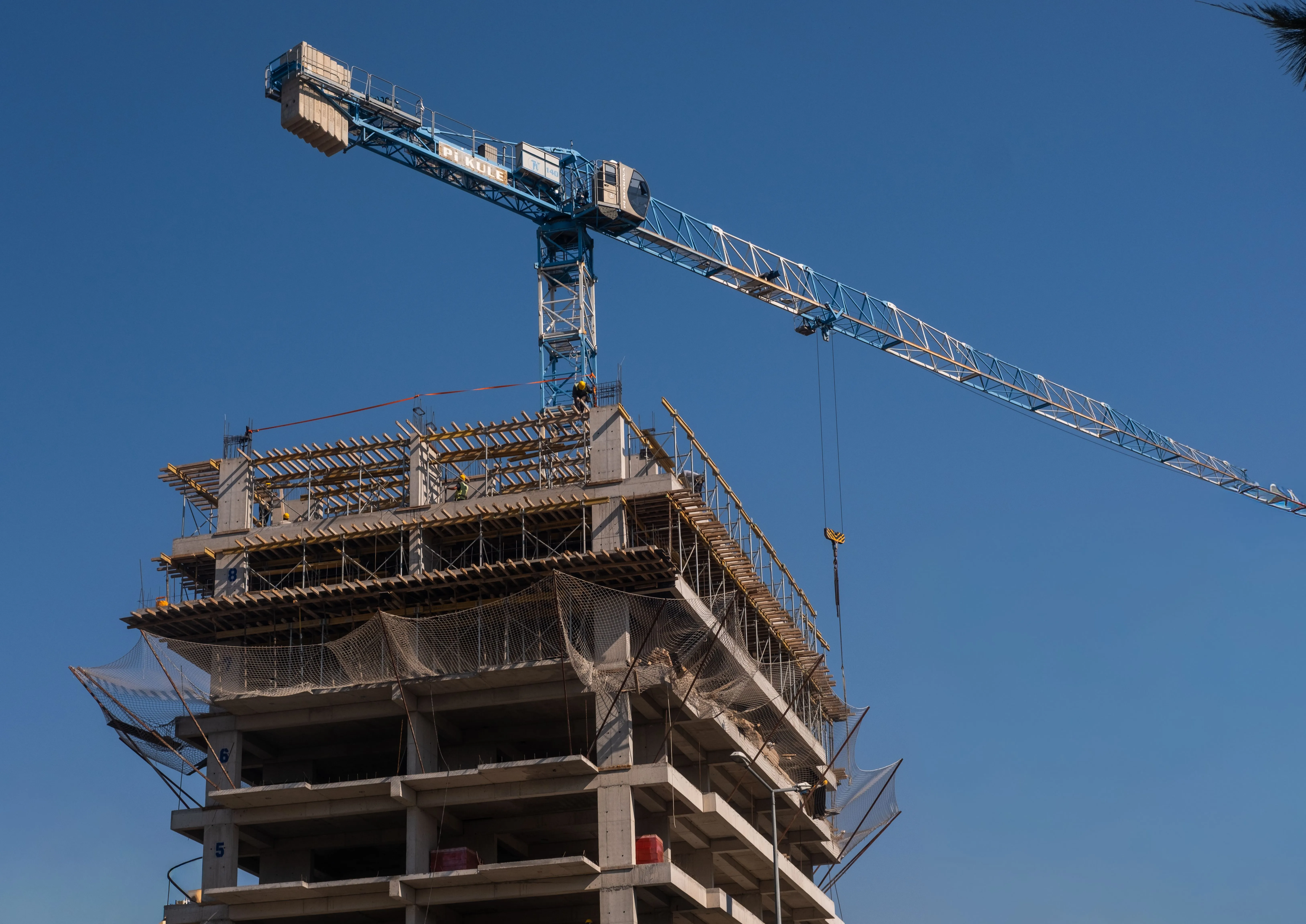 Guindaste opera em edifício em construção sob céu azul.