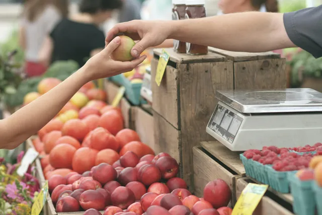 Pessoa entrega fruta em feira com bancas de alimentos frescos