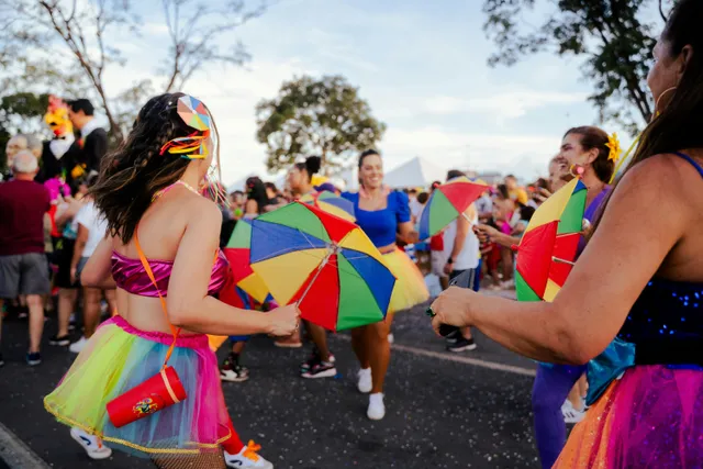 Pessoas dançam com fantasias coloridas e sombrinhas em festa de rua