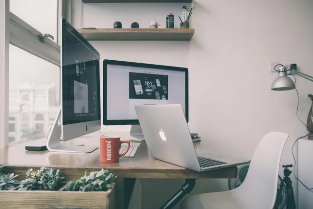 Estação de trabalho moderna com dois monitores, laptop e xícara de café