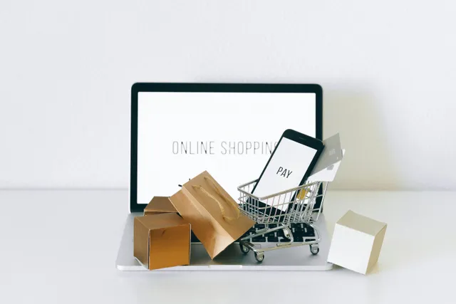 Carrinho com celular e sacolas em frente a tela com 'online shopping'