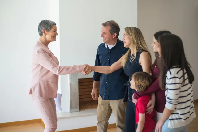 #FotoDescrição: Mulher cumprimentando uma família sorridente em um ambiente residencial, representando um atendimento próximo e humanizado.